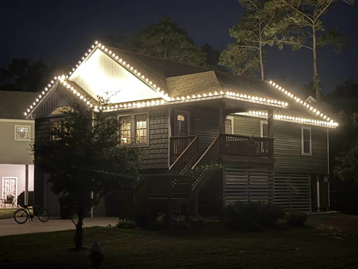 Outer Banks beach house roofline lit with warm white holiday lights at night, installed by Top Shelf OBX
